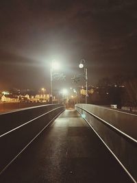 Illuminated street lights on road against sky at night