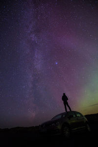 Silhouette hiker standing on car against starry field at night