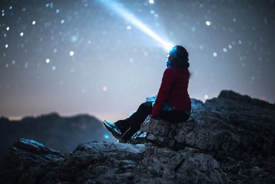 Woman wearing headlamp sitting on rock against sky