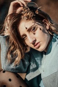 Portrait of beautiful young woman holding dried plant while sitting outdoors