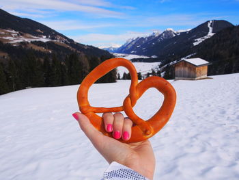 Cropped hand of woman holding pretzel over snow against sky