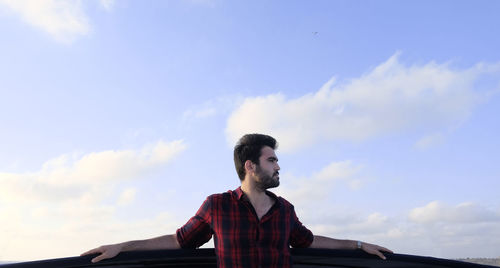 Portrait of young man looking away against sky