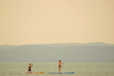 Women paddleboarding in sea against clear sky