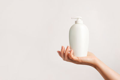 Cropped hand of woman holding bottle against white background