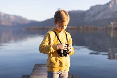 Boy looking at binoculars by lake