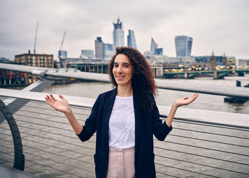 Portrait of smiling young woman standing in city against sky