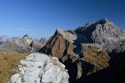 Rear view of person walking on rocks against blue sky