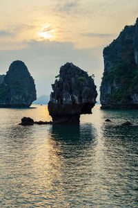 Rock formation in sea against sky during sunset