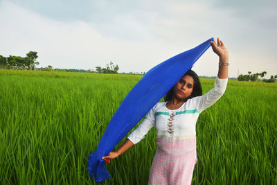 Woman with arms raised standing on field against sky