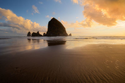 Rock formation on beach against sky during sunset