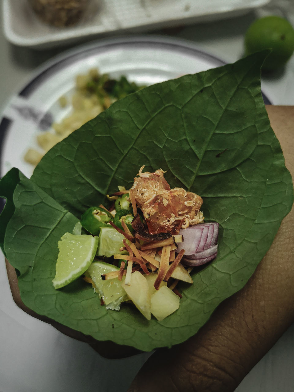 CLOSE-UP OF HAND HOLDING LEAF IN PLATE