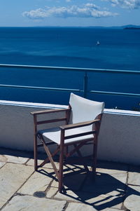 Chair on table by sea against blue sky