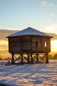 Built structure on snow covered field against sky during sunset