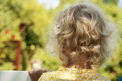 Little girl with blonde curly hair looking away in the garden.