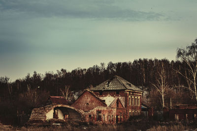 Old house on field by trees against sky