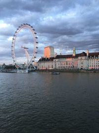 View of ferris wheel in city against cloudy sky