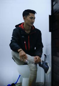 Young man looking away while sitting on wall