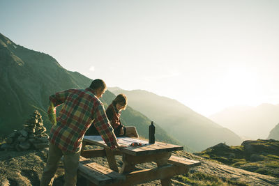 Couple reading map on picnic table against mountains during sunset