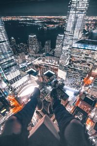 Low section of person sitting on building terrace about towers in illuminated city