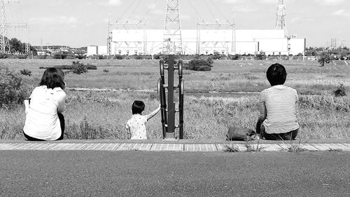 Rear view of mother and daughter sitting on electricity pylon