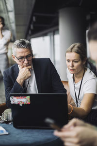 Contemplating businessman by female coworker working on laptop in office corridor