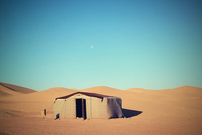 Scenic view of hut on sand dunes in desert against clear sky