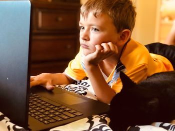 Cute boy using laptop while lying on bed at home