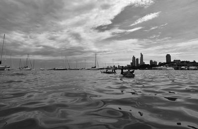 Sailboats in sea by modern buildings against sky