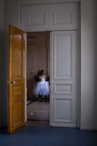 Young woman wearing tutu using mobile phone seen through doorway