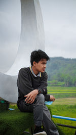 Full length of man sitting on field against sky