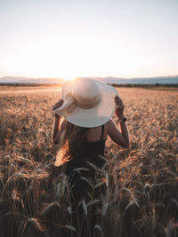 Rear view of woman standing on wheat field at sunset