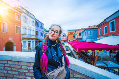 Portrait of young woman standing against buildings in city