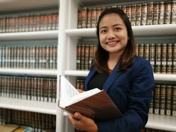 Portrait of smiling lawyer holding book in library