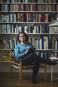 Portrait of female therapist holding digital tablet while sitting against bookshelf
