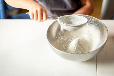 A close view of the hand of the child sifting flour