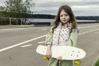 Portrait of a beautiful caucasian girl standing on road with a skate board. 