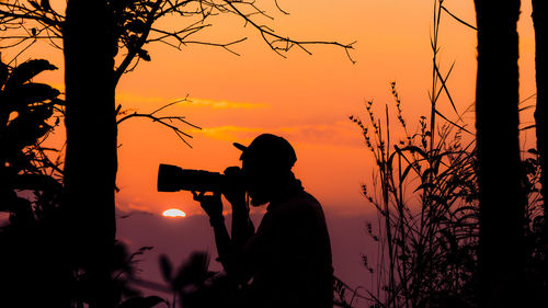 Silhouette man photographing against sky during sunset