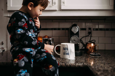 Young boy sitting on counter top with spilled milk on coffee cup