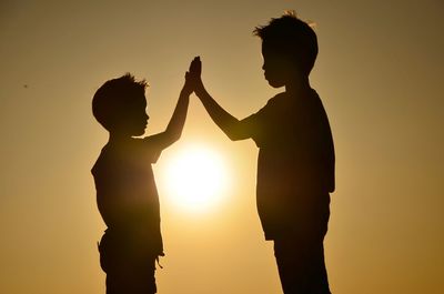 Silhouette people giving high-five while standing against sky during sunset