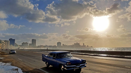 Cars on city by sea against sky during sunset