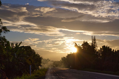 Road by trees against sky during sunset