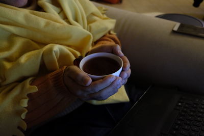 Midsection of woman holding coffee cup with laptop