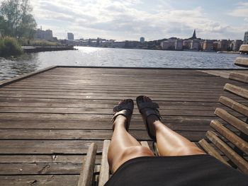 Low section of woman relaxing on river against sky