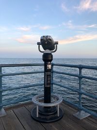 Coin-operated binoculars by sea against sky during sunset