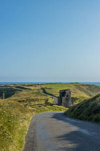 Road passing through landscape against clear blue sky