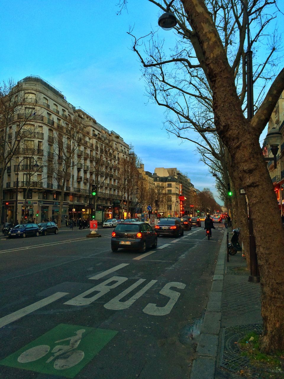 architecture, building exterior, transportation, built structure, car, road, street, road marking, land vehicle, city, the way forward, sky, mode of transport, city street, incidental people, clear sky, city life, tree, day, blue