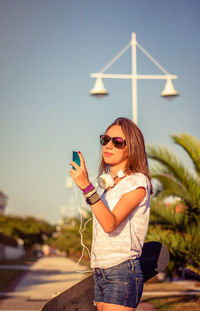 Young woman using mobile phone against sky