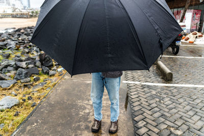 Low section of woman with umbrella walking on street