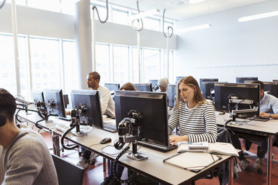 Male and female young students using computers at desk in university library