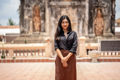 Portrait of young woman standing against building